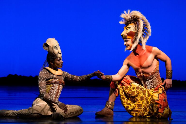 Blauer Hintergrund und davor 2 Personen die Simba und Nala darstellen