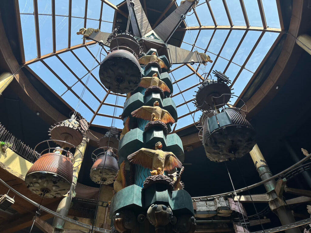 Blick nach oben zur reich verzierten Mittelsäule von Winja's mit geflügelten Enten-Figuren und hängenden Gondeln unter dem gläsernen Kuppeldach.